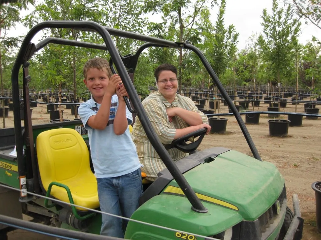 Woman and young boy smiling in a John Deere utility vehicle among nursery rows
