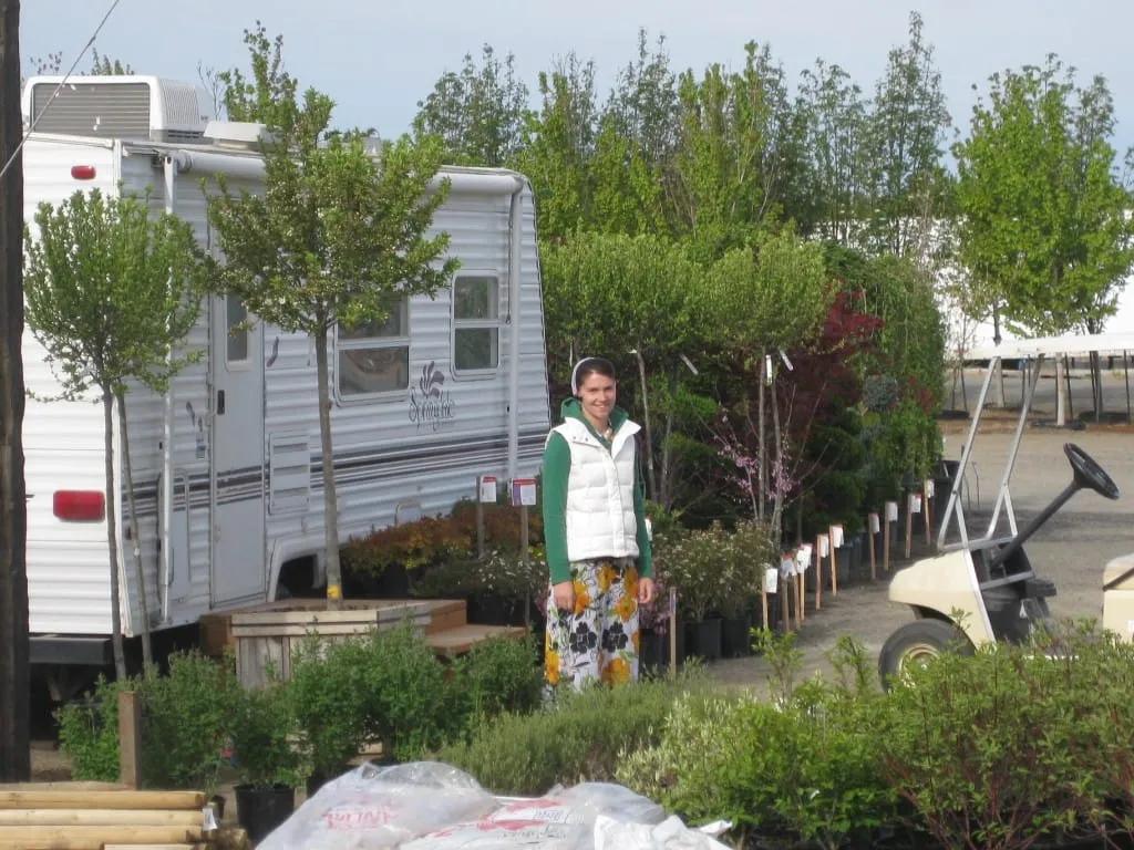 Woman standing among potted nursery plants near a travel trailer