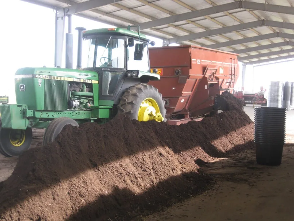John Deere tractor and hopper unloading a large pile of soil under the barn