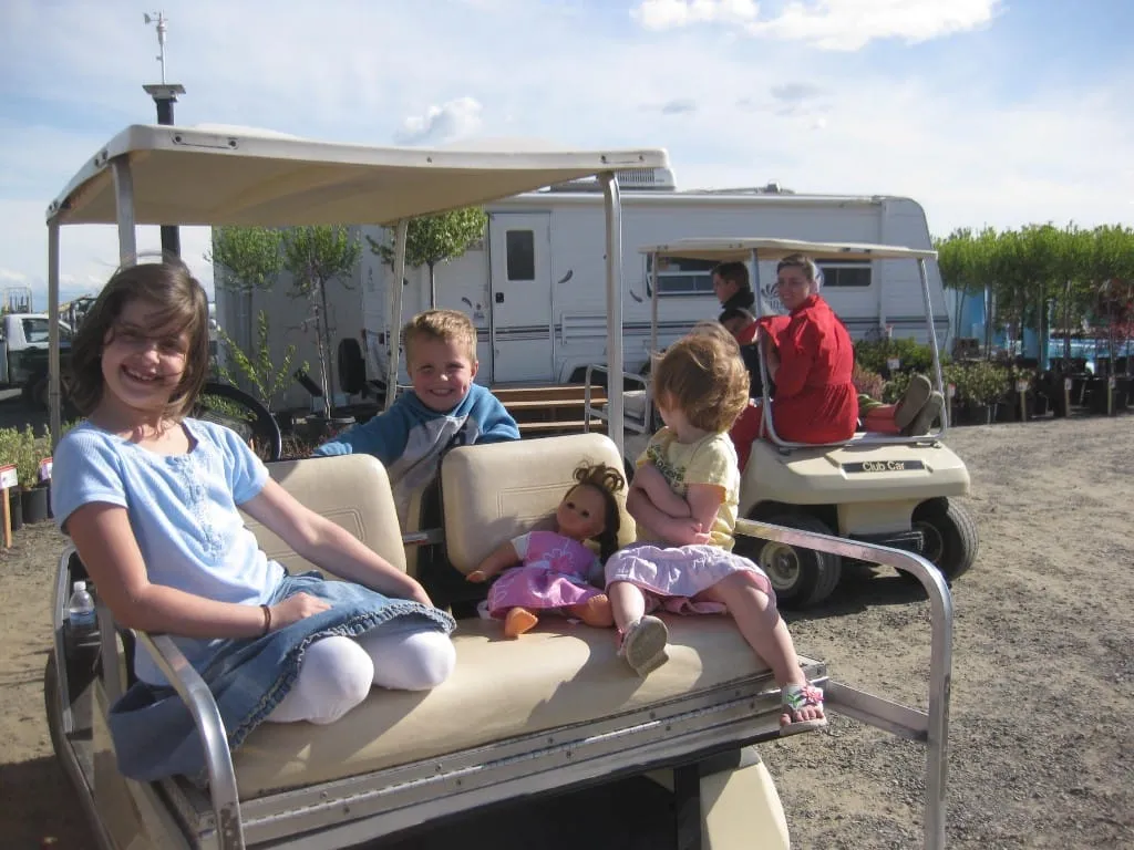Children in a golf cart with an RV and nursery rows behind them