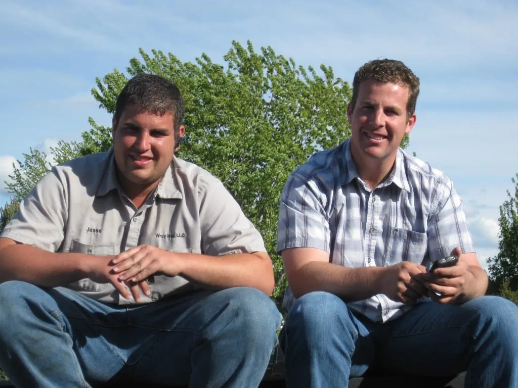 Two men sitting outdoors under a clear sky and green tree