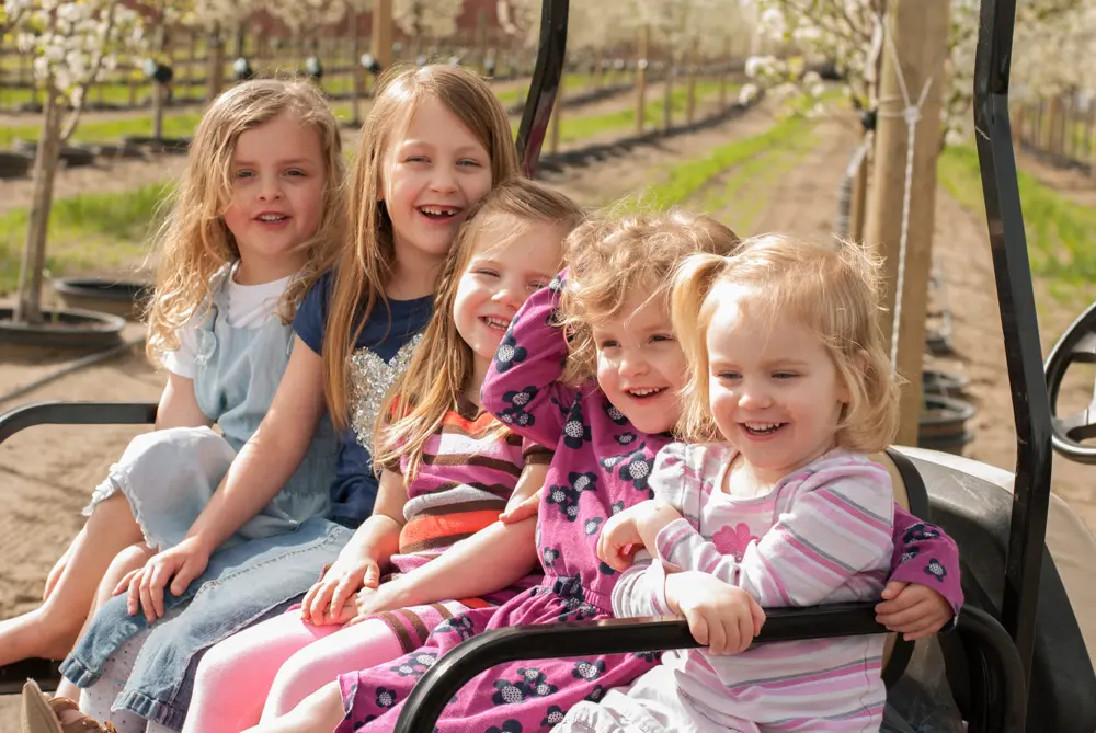Five girls smiling from the back of a utility cart among spring blossoms